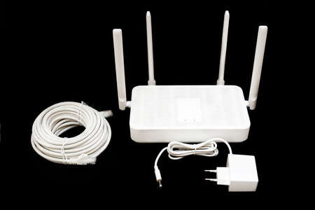 Dual band WiFi 6 router with a power supply adapter and a roll of cable isolated on black.