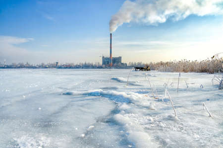 View of the smoking chimney of the waste incineration plant from the frozen pond. Pollution produced by burning garbage.の写真素材