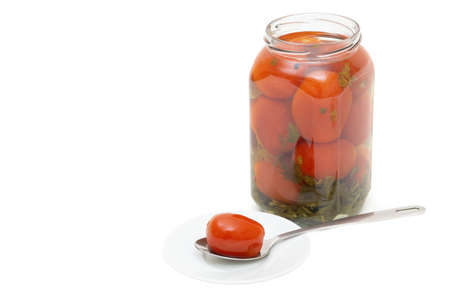 Pickled tomato in a spoon on a white saucer by the jar of salted plum tomatoes isolated on whiteの写真素材
