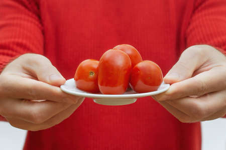 Man in a red sweater holding a white saucer with pickled tomatoes close to the cameraの写真素材