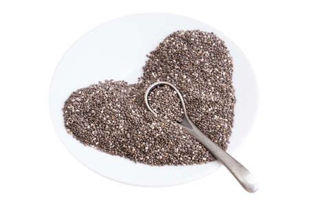 Heart symbol made of chia seeds on a white plate with a small spoon isolated on whiteの写真素材