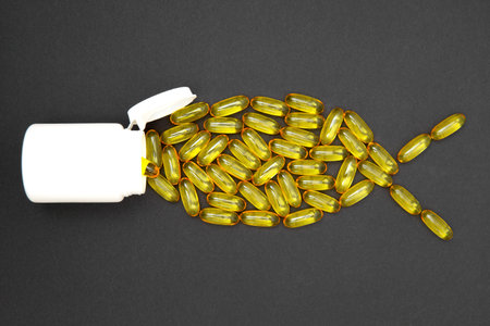 Omega-3 fish oil softgels arranged into a fish shape swimming inside a white pharmacy bottle on a black background.の写真素材