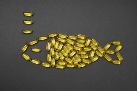 Omega-3 fish oil capsules arranged into a fish symbol on a black background. Fatty acids benefits...