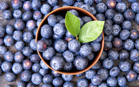 Wooden bowl full of fresh blueberries and green leaves on top of a scattered berries background. Healthy organic dessert concept.の写真素材