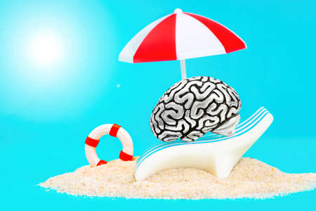 Miniature human brain relaxing on a sunbed under a sun umbrella on a sandy beach. Psychological...
