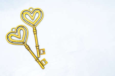 Two vintage style gold toned heart shaped keys on a neutral background.の写真素材
