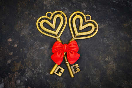 Crossed antique style skeleton keys with a red bow on a dark grungy table. Symbolic romantic...