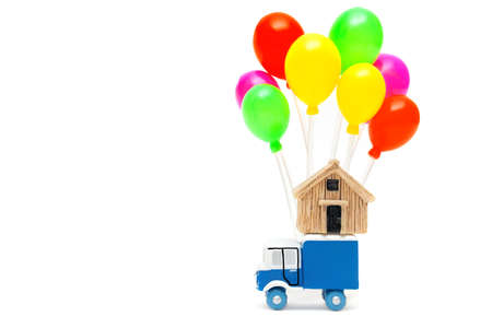 Toy truck with a miniature house model and a cluster of multicolored balloons isolated on white...