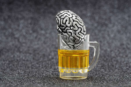 Anatomical copy of a human brain in a miniature beer mug against a gray background. Alcohol and mental health concept.の写真素材