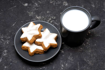 Plate of cinnamon star cookies and a cup of milk left for Santa on a textured black table. Christmas food custom concept.の写真素材