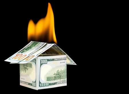 Burning house made from one hundred dollar bills isolated on black background. Creative fire and...