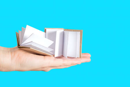 Two miniature handmade books with blank pages in hand isolated on blue background. Studying and...