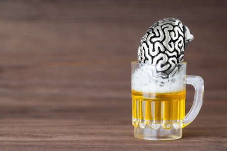 Anatomical steel copy of a human brain in a miniature beer mug against a wooden background. Drowning grief and problems in alcohol.の写真素材