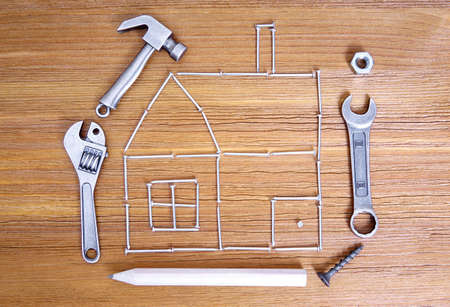 House shape made from nails, hand tools and fasteners on a wooden background. Home repair tips and tricks concept.の写真素材