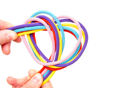 Crop view of female hands twisting five multicolored braided cords into a heart shape against a...