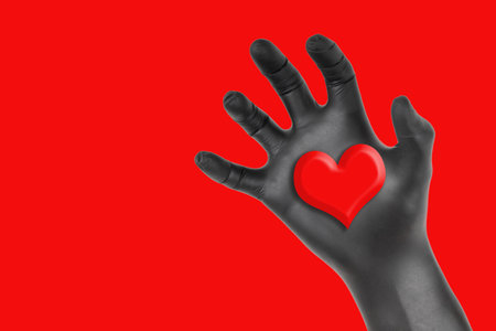 Black gloved hand grabbing a heart isolated on a red background. Romantic heart stealing concept.の写真素材