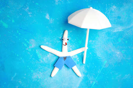 Happy white starfish character floating on a light blue background with a white parasol in hand. Positive sea vacation concept.の写真素材