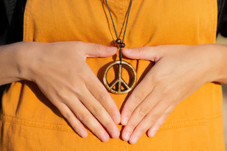 Hands making a heart symbol around a peace sign pendant. Anti-war concept.の写真素材
