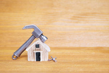 Small steel hammer and nails by a miniature toy house against a wooden background. Home renovation...