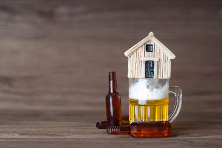 Miniature wooden house model standing on top of a small beer mug with empty bottles lying around....