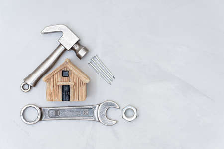 Miniature toy house, small hammer, wrench, nut and nails on a concrete table background. Household maintenance and repair concept.の写真素材