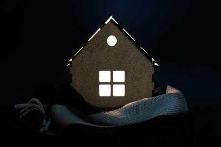 Miniature house model wrapped with a scarf and illuminated from inside. Creative house insulation concept.の写真素材