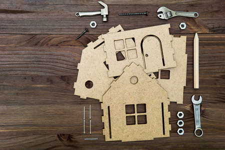 Parts of a cardboard house model with a set of miniature hand tools and fasteners arranged around on a wooden background with copy space.の写真素材