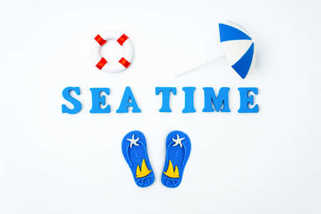 Summer vacation background: lettering SUMMER TIME made of wooden characters, toy lifebuoy, flip flops and a sun umbrella isolated on white.の写真素材