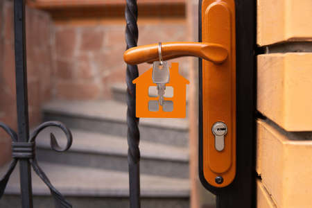 Crop view of a residence entrance door and a key with a flat house shaped wooden keychain hanging on...