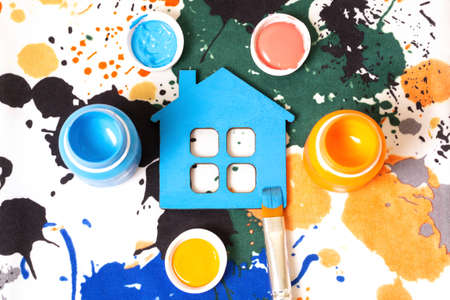 Freshly painted flat blue house with paint bottles and a brush on a stained watercolor fabric background. Interior renovation and refreshment concept.の写真素材