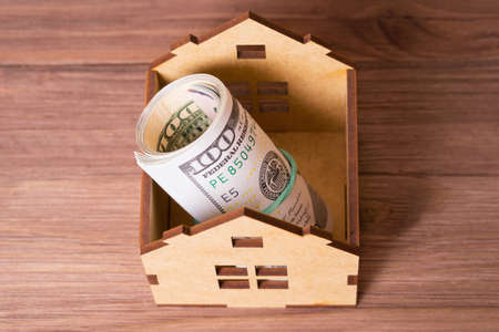 One hundred dollar bills cash roll inside a miniature wooden house model. House buying concept.の写真素材