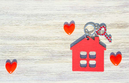 Key decorated with rhinestones, red house shaped keychain and small hearts on a wooden background....
