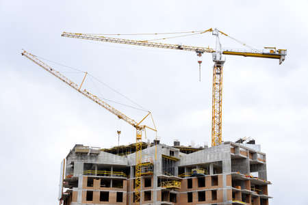 House construction site with two tower cranes against sky background.