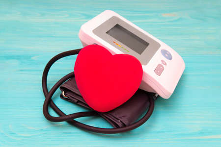 Blood pressure monitor and a large red heart shape on a turquoise background. Heart disease...