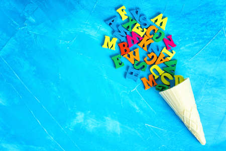 Bunch of colorful wooden letters coming out from a waffle cone isolated on a blue textured background with copy space.の写真素材