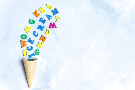 Ice cream shape made from a waffle cone and multicolored letters arranged on a concrete background.の写真素材