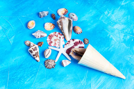 Waffle cone and seashells arranged into an ice cream shape on blue background imitating water. Vivid summer vacation concept.の写真素材