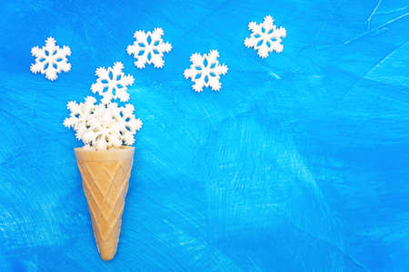 Waffle cone and white snowflake shapes arranged on a blue textured background with copy space.の写真素材