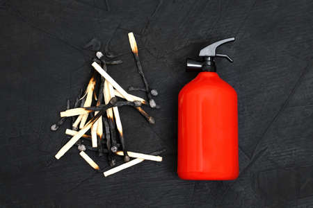 Tiny red fire extinguisher placed by a pile of burnt matches on black background, top view.の写真素材