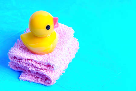 Baby rubber duck placed on a pile of miniature bath towels isolated on blue background. Bath time fun concept.の写真素材