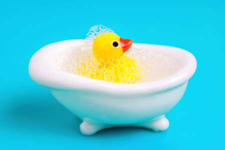 Toy yellow duck in a miniature white bathtub covered with soap bubbles. Bath time concept.