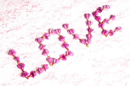 Word LOVE made from pink acacia flowers. Clean and delicate floral background.