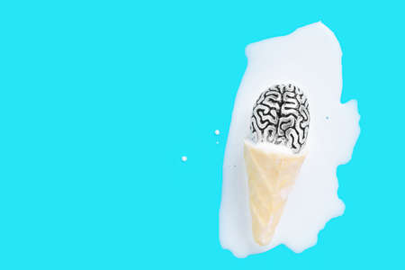 Steel copy of a human brain in melted waffle cone ice cream puddle on a blue background with copy...