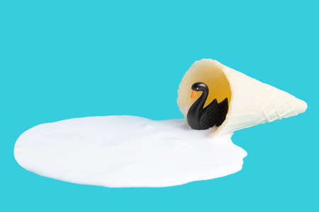 Black swan figurine swimming in a melted waffle cone ice cream puddle isolated on blue background.の写真素材