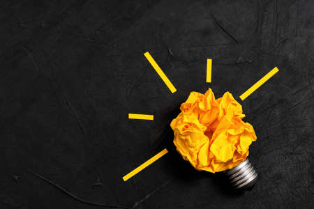 Glowing lightbulb shape made from a crumpled paper ball and a base. Creative process concept.