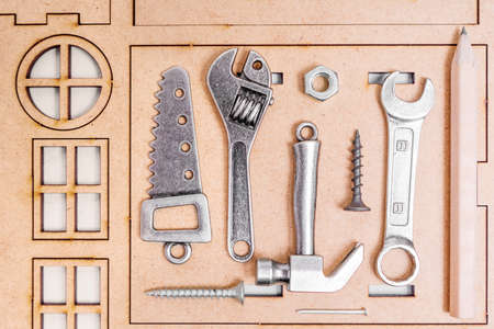 Set of miniature tools and fasteners to build a house arranged on a wooden home model kit.