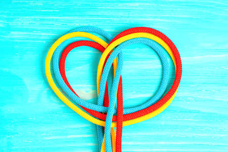 Red, yellow and blue braided cords tied into a heart shape on a wooden background. Creative teamwork concept.の写真素材