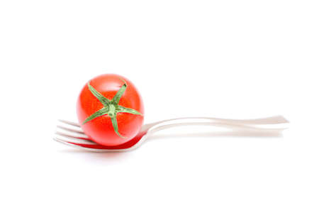 Close-up of a cocktail tomato placed on top of a miniature fork isolated on white background.の写真素材