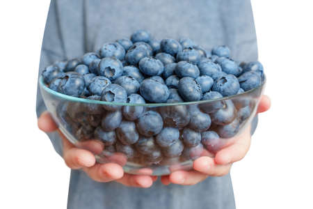 Woman wearing a matching dress holds a large glass bowl of fresh ripe blueberries isolated on white background, wide angle, selective focus.の写真素材