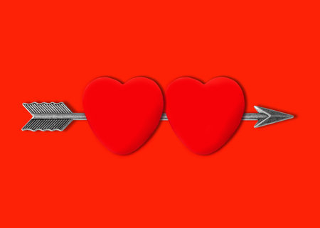 Feathered bow arrow passing through two heart shapes isolated on red background with copy space.の写真素材